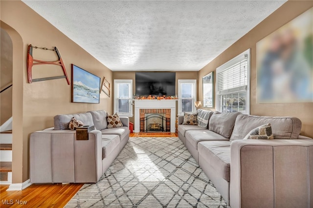 living room with hardwood / wood-style flooring, a textured ceiling, and a brick fireplace