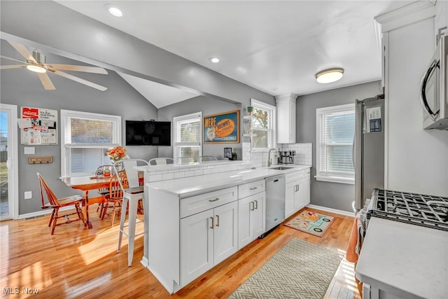 kitchen featuring stainless steel appliances, kitchen peninsula, lofted ceiling, a breakfast bar, and white cabinets