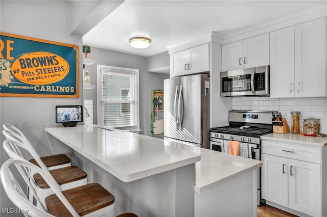 kitchen with white cabinets, appliances with stainless steel finishes, a kitchen bar, and kitchen peninsula