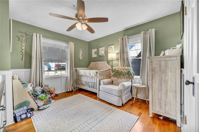 bedroom featuring ceiling fan, light wood-type flooring, multiple windows, and a nursery area