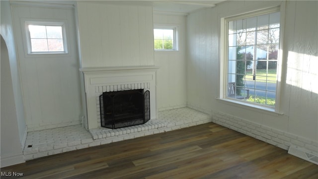 unfurnished living room featuring a brick fireplace, wood walls, and dark hardwood / wood-style flooring