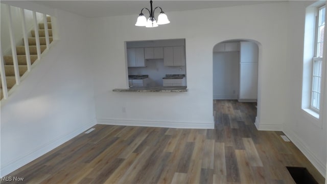 kitchen with light stone counters, kitchen peninsula, a notable chandelier, dark wood-type flooring, and pendant lighting