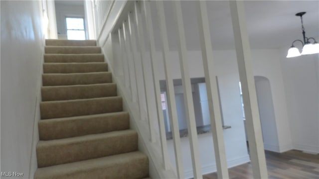 stairway with hardwood / wood-style flooring and a notable chandelier