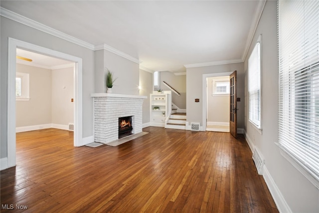 unfurnished living room featuring hardwood / wood-style flooring, ornamental molding, and a brick fireplace