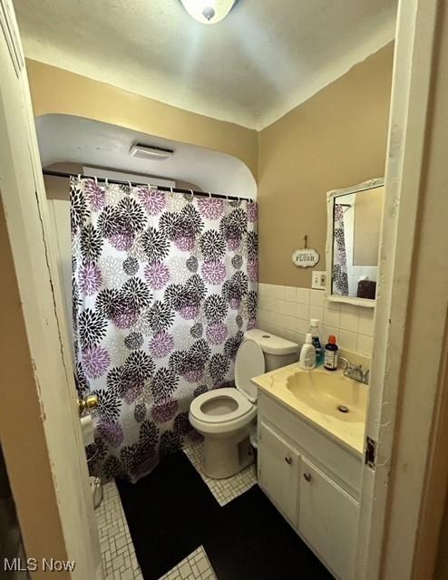 bathroom featuring tile patterned flooring, vanity, toilet, and tile walls