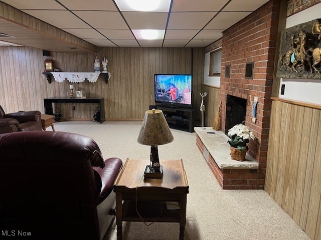 carpeted living room with a drop ceiling, a fireplace, and wooden walls