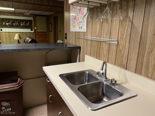 kitchen featuring tile patterned flooring, wood walls, and sink