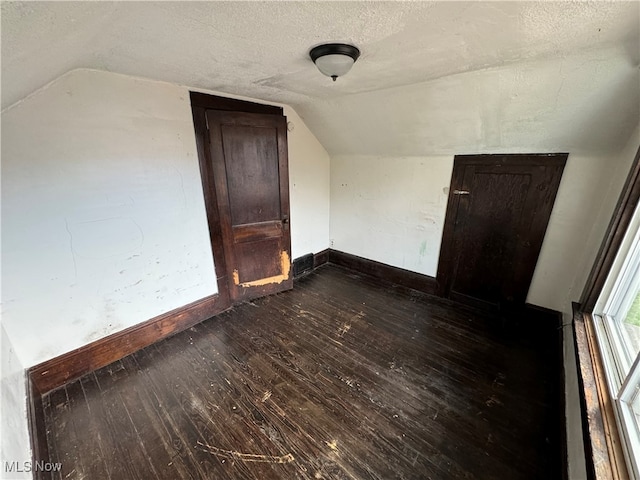 additional living space featuring vaulted ceiling, a textured ceiling, and dark hardwood / wood-style flooring