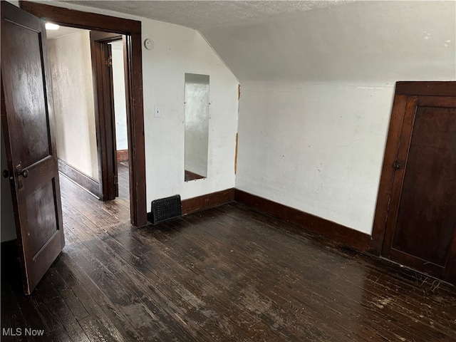 unfurnished room featuring dark hardwood / wood-style flooring, a textured ceiling, and vaulted ceiling