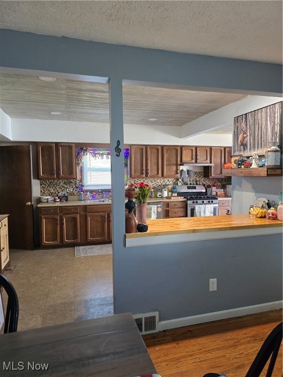 kitchen with tasteful backsplash, wood-type flooring, a textured ceiling, dark brown cabinets, and stainless steel range with gas stovetop