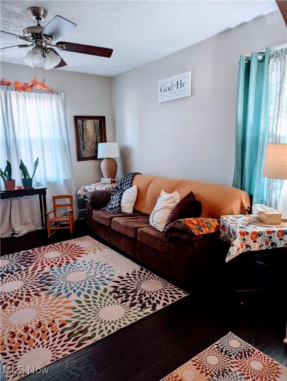 living room with dark wood-type flooring, ceiling fan, and a textured ceiling