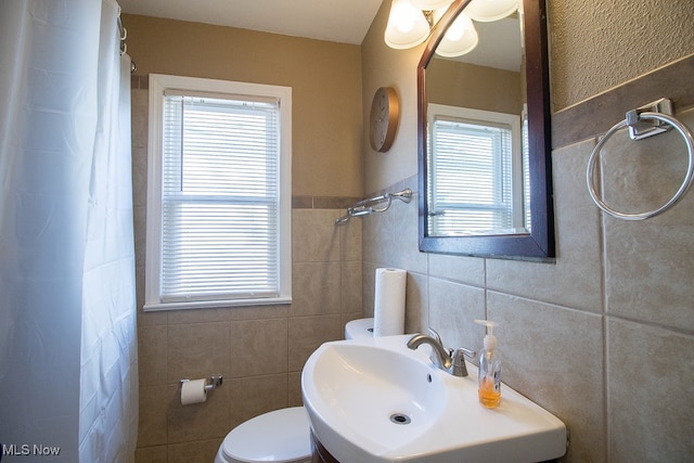 bathroom featuring tile walls, curtained shower, sink, and toilet