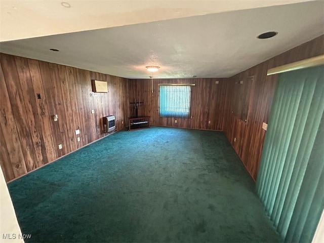 spare room featuring wood walls, heating unit, and dark colored carpet