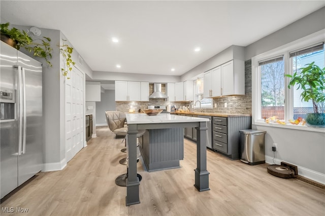 kitchen featuring backsplash, wall chimney range hood, light wood-type flooring, appliances with stainless steel finishes, and white cabinetry