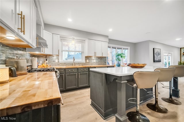 kitchen featuring gray cabinetry, light hardwood / wood-style flooring, extractor fan, a breakfast bar area, and a kitchen island