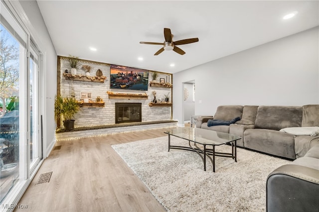 living room featuring a brick fireplace, ceiling fan, and light wood-type flooring