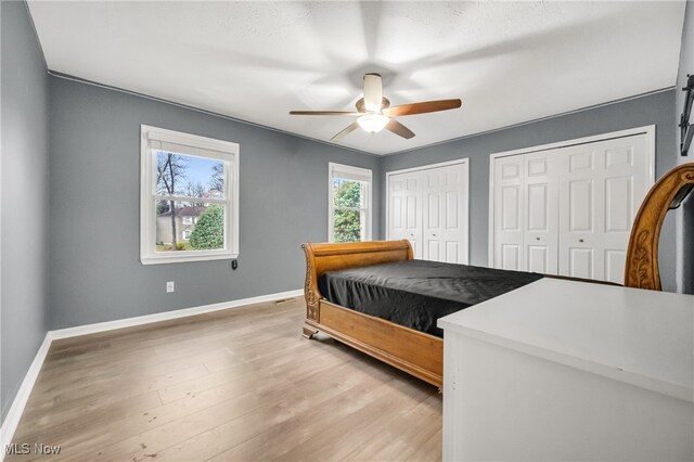 bedroom with ceiling fan, wood-type flooring, and two closets