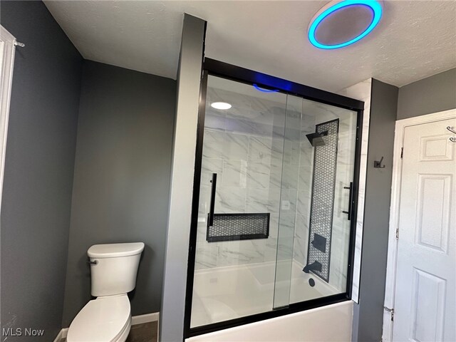 bathroom featuring toilet, enclosed tub / shower combo, and a textured ceiling