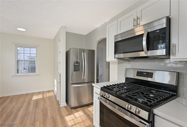 kitchen featuring white cabinets, backsplash, light hardwood / wood-style floors, and stainless steel appliances