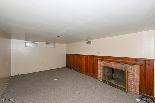 basement with light carpet, wooden walls, and a brick fireplace