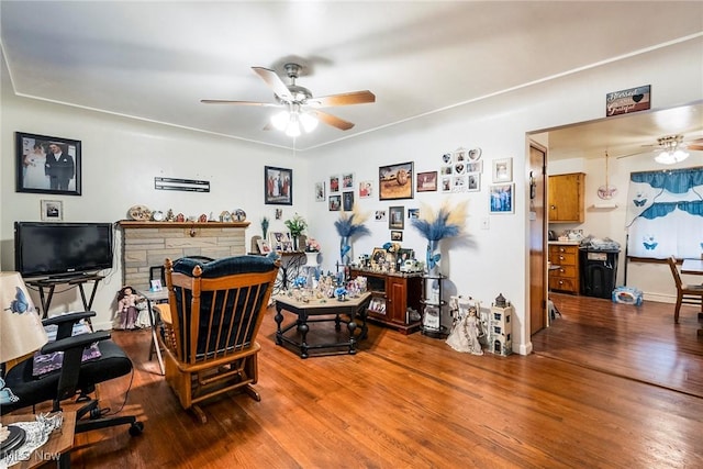 home office with ceiling fan, a stone fireplace, and wood-type flooring