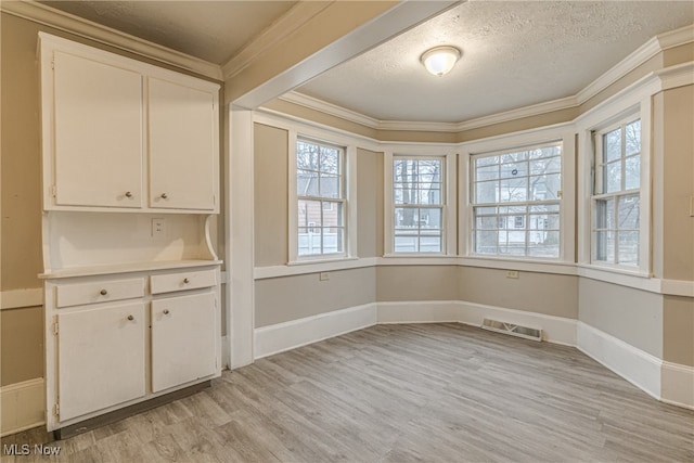 unfurnished dining area featuring light wood-type flooring, a wealth of natural light, a textured ceiling, and ornamental molding