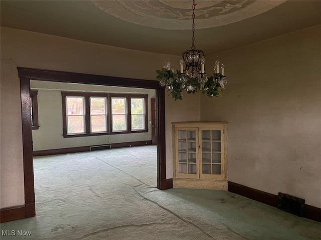 spare room featuring light carpet and an inviting chandelier