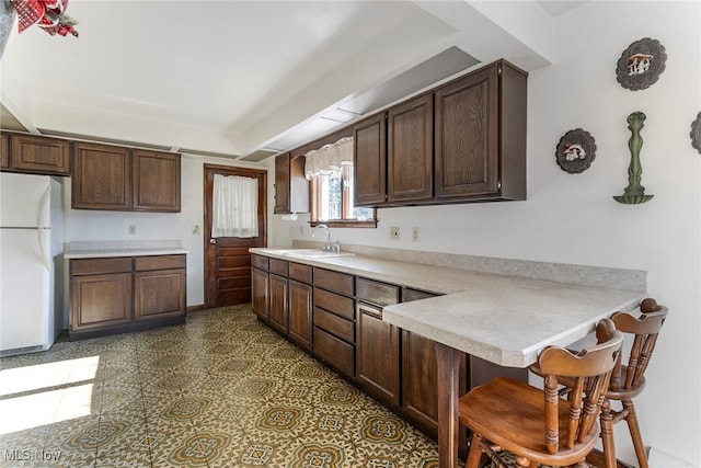 kitchen with sink, a breakfast bar, kitchen peninsula, dark brown cabinets, and white fridge