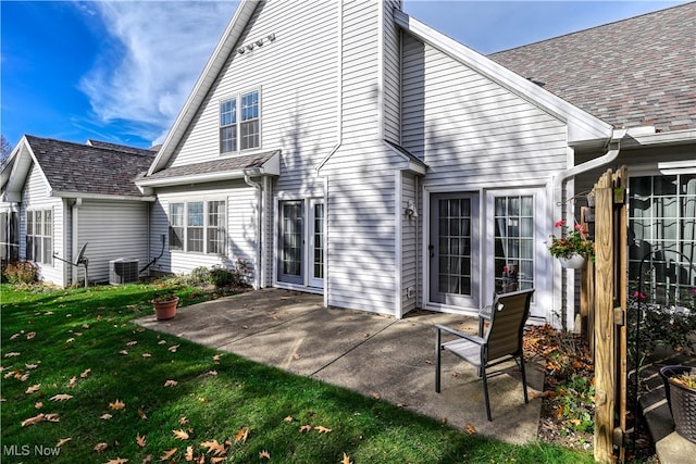 back of house with a yard, central air condition unit, a shingled roof, and a patio