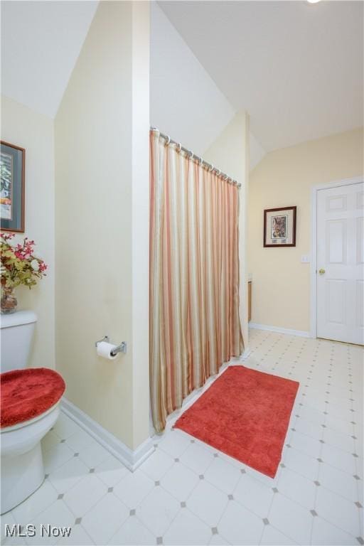 bathroom featuring lofted ceiling, toilet, baseboards, and tile patterned floors