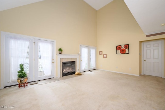 unfurnished living room with visible vents, baseboards, a tiled fireplace, carpet flooring, and high vaulted ceiling