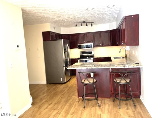 kitchen featuring kitchen peninsula, appliances with stainless steel finishes, a kitchen breakfast bar, and light hardwood / wood-style flooring