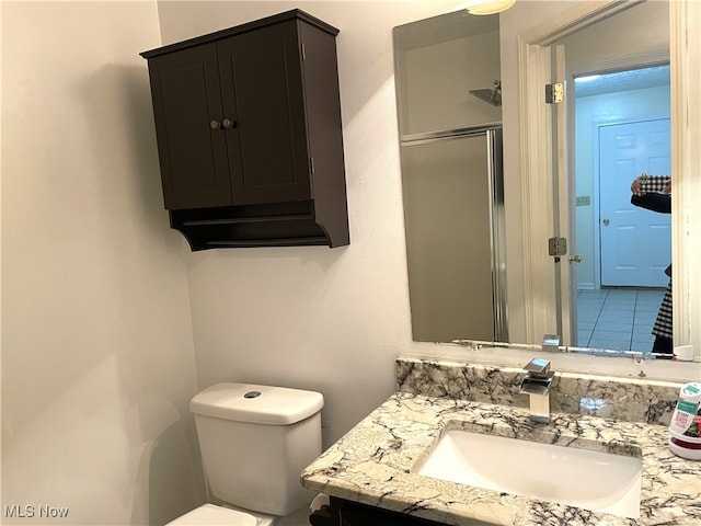 bathroom with a shower with door, vanity, toilet, and tile patterned flooring