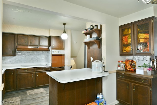 kitchen featuring kitchen peninsula, backsplash, hanging light fixtures, white appliances, and light wood-type flooring