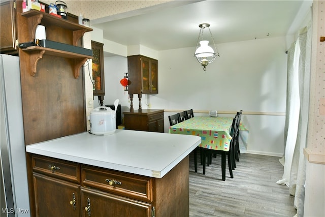 kitchen with refrigerator, kitchen peninsula, hanging light fixtures, dark brown cabinets, and light hardwood / wood-style flooring