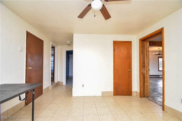 tiled spare room with ceiling fan with notable chandelier