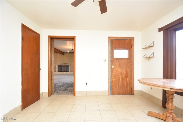 interior space with a brick fireplace, ceiling fan, and light tile patterned floors