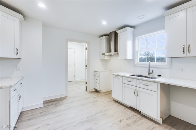 kitchen featuring white cabinets, light hardwood / wood-style floors, wall chimney range hood, and sink