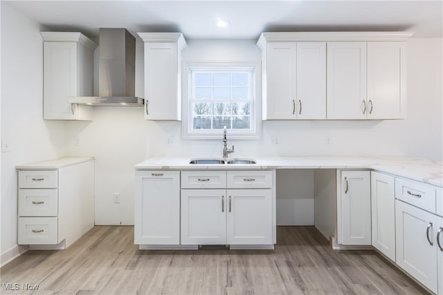 kitchen with white cabinets, sink, wall chimney exhaust hood, and light hardwood / wood-style flooring