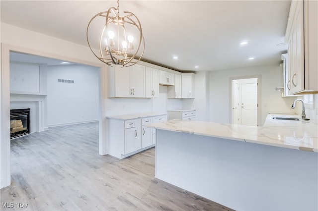 kitchen featuring light hardwood / wood-style floors, pendant lighting, an inviting chandelier, sink, and white cabinetry