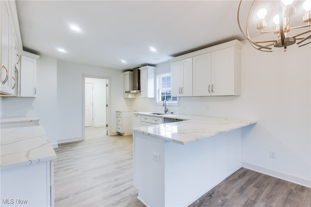 kitchen with an inviting chandelier, white cabinets, wall chimney exhaust hood, sink, and light wood-type flooring