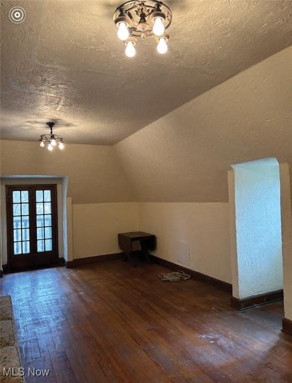 bonus room with vaulted ceiling, dark wood-type flooring, an inviting chandelier, and french doors