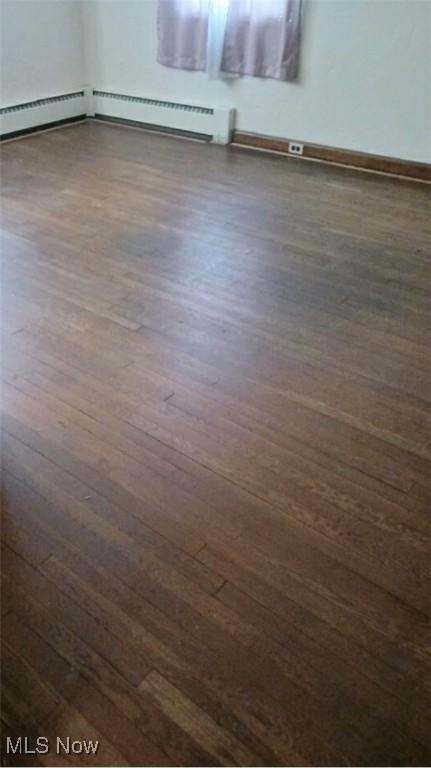 empty room featuring dark wood-type flooring and a baseboard radiator