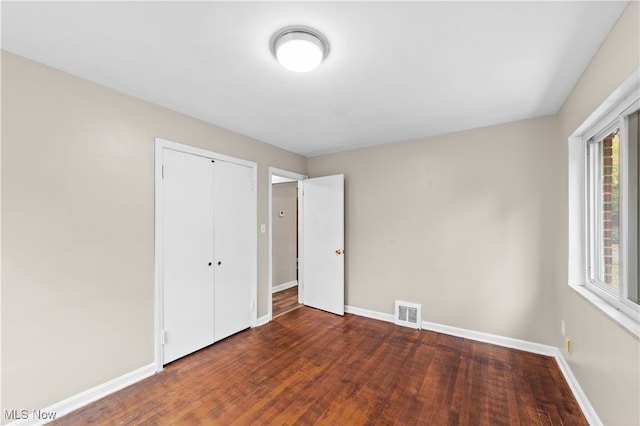 unfurnished bedroom with dark hardwood / wood-style flooring, a closet, and multiple windows