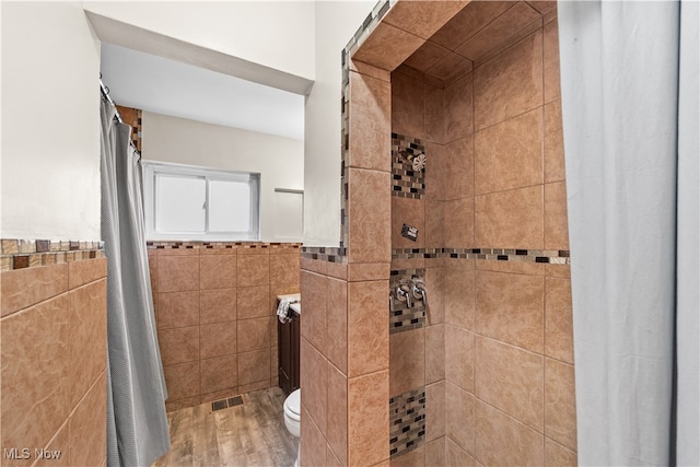 bathroom featuring a shower with shower curtain, toilet, and tile walls