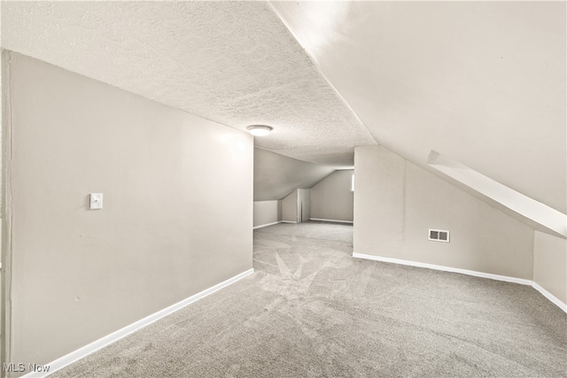 additional living space with a textured ceiling, light colored carpet, and vaulted ceiling