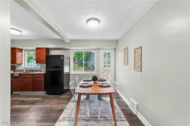 dining room featuring dark wood-type flooring, beam ceiling, sink, and a textured ceiling