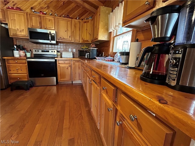 kitchen featuring light hardwood / wood-style floors, appliances with stainless steel finishes, wood ceiling, vaulted ceiling with beams, and butcher block countertops