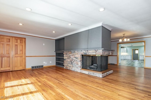 unfurnished living room featuring a fireplace, an inviting chandelier, light hardwood / wood-style flooring, and ornamental molding