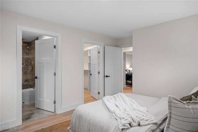 bedroom with light hardwood / wood-style floors, connected bathroom, and a spacious closet